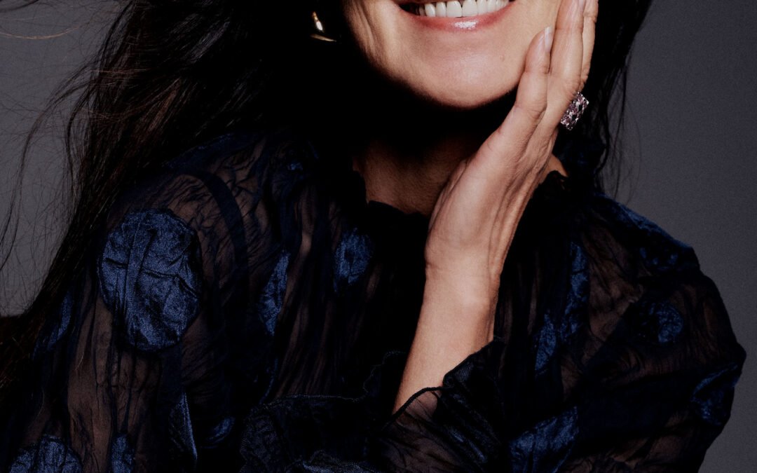 Portrait en studio d’un modèle souriant, une main ornée d’une bague près du visage.